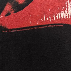 Puede incluir: Una camiseta negra con una imagen roja y blanca de un par de labios. El texto "TM & &copy; 1975, 2013 Twentieth Century Fox Film Corporation, All Rights Reserved." est&aacute; impreso en la parte inferior de la camiseta.