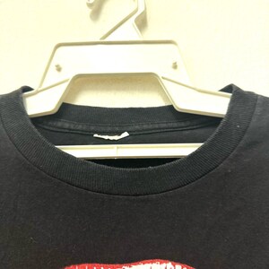 Puede incluir: Primer plano del cuello de una camiseta negra con un estampado gr&aacute;fico rojo y blanco de un par de labios.
