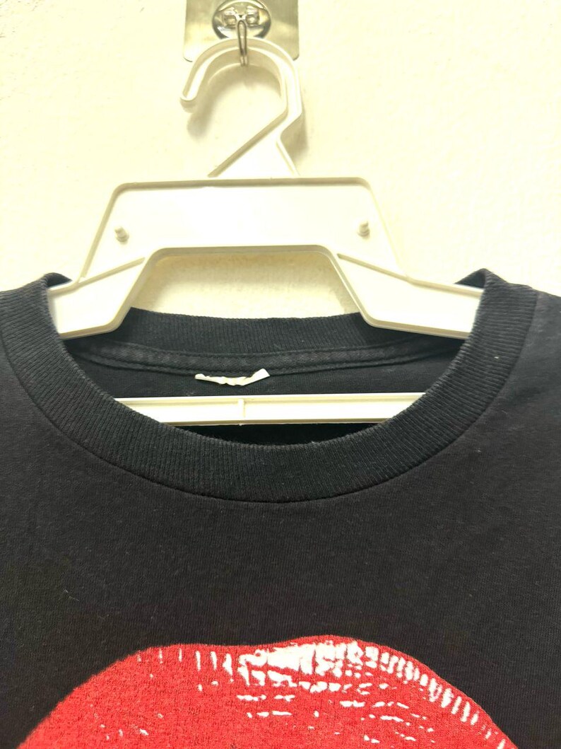 Puede incluir: Primer plano del cuello de una camiseta negra con un estampado gr&aacute;fico rojo y blanco de un par de labios.