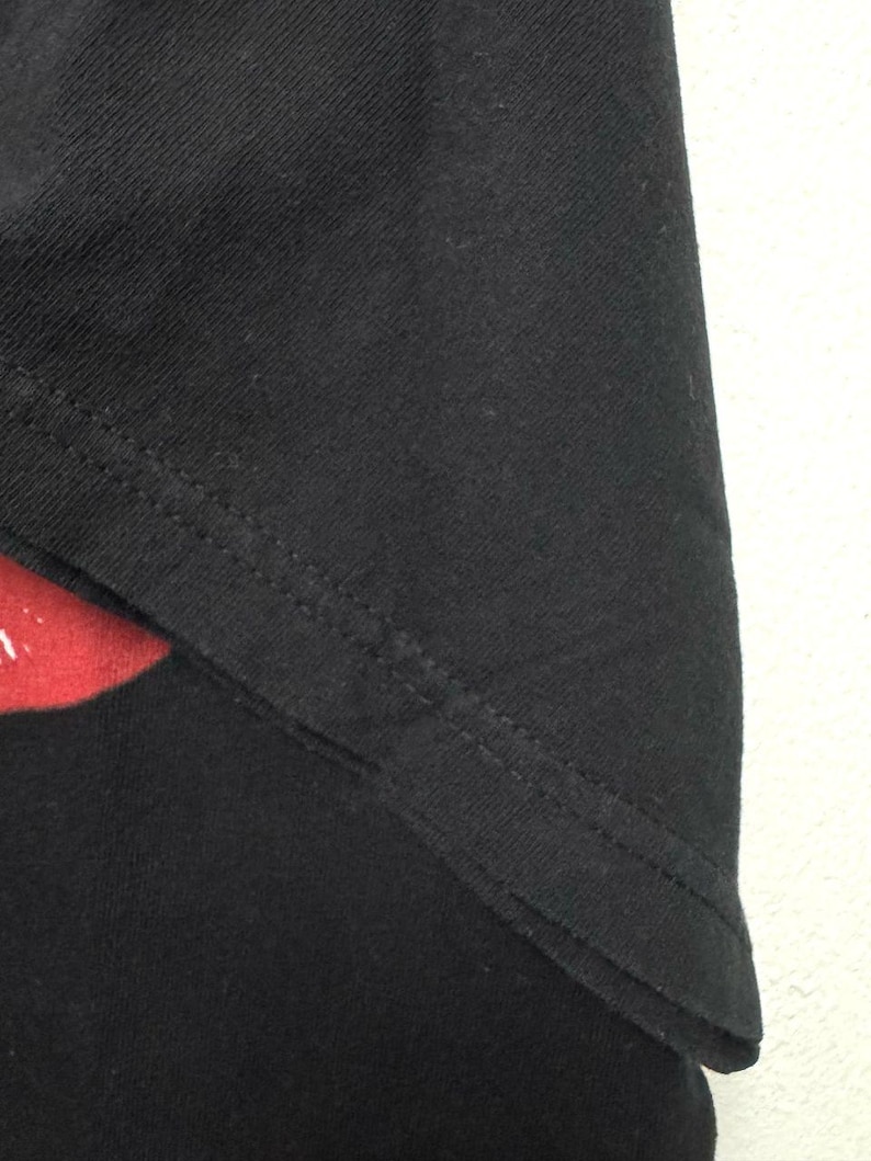 Puede incluir: Primer plano de la costura de tela negra de una camiseta negra. La costura est&aacute; cosida con una puntada recta.