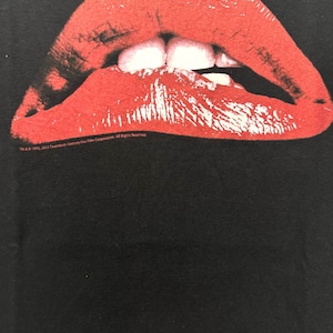 Puede incluir: Una camiseta negra con una imagen roja, blanca y negra de un par de labios. Los labios est&aacute;n abiertos y los dientes son visibles. El texto "TM & &copy; 1982, 2012 Twentieth Century Fox Film Corporation. All Rights Reserved." est&aacute; impreso en la parte inferior de la imagen.