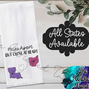 May include: White kitchen towel with the text "Miles Apart But Close At Heart" and two state outlines connected by a dotted line with a heart. The text "All States Available" is also displayed.