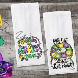 May include: Two white kitchen towels with Mardi Gras themed designs. One towel features a purple, green, and gold beaded necklace with the text "We Don't Hide The Crazy We Parade It". The other towel features a purple, green, and gold king cake with the text "King Cake Calories Don't Count".