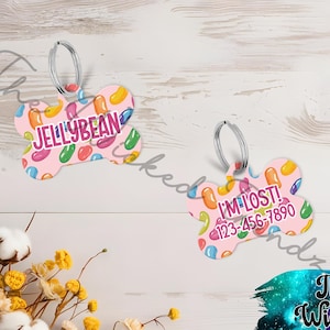 May include: Two bone-shaped pet tags with a pink background and colorful jelly bean graphics. One tag reads "JELLYBEAN" in pink and white text. The other tag reads "I'M LOST!" with a phone number.
