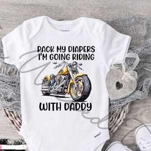 May include: White baby onesie with the text "Pack my diapers I'm going riding with Daddy" and a yellow motorcycle graphic. Includes a pair of white baby shoes.