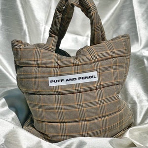May include: A brown and tan quilted tote bag with a white label that says "PUFF AND PENCIL".