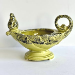 May include: A green ceramic bowl with a black swirl design. The bowl has a bird-shaped handle and a pedestal base.