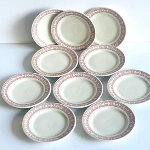 May include: A collection of cream-colored plates with a decorative red border. The set includes both round and oval-shaped plates, ideal for serving meals. The plates are arranged on a white surface.
