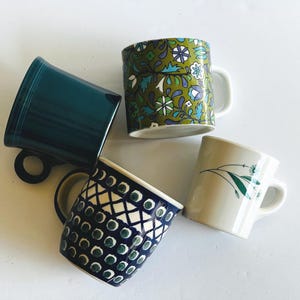 May include: Four ceramic mugs in various designs. One is teal, another has a floral pattern in green, blue, and white. A third mug features a blue and white geometric design, and the last has a simple green floral design.