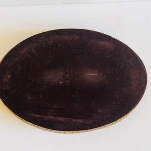 K&ouml;nnte beinhalten: Ein ovales Tablett mit schwarzem Samtbezug und einem goldenen Metallrand. Das Tablett hat ein dekoratives Muster am Rand.