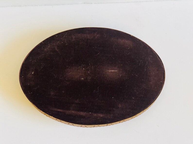 K&ouml;nnte beinhalten: Ein ovales Tablett mit schwarzem Samtbezug und einem goldenen Metallrand. Das Tablett hat ein dekoratives Muster am Rand.