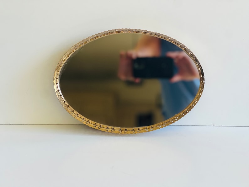 K&ouml;nnte beinhalten: Ein goldfarbenes, ovales Tablett mit einer Spiegelfl&auml;che und einem dekorativen, verzierten Rand.