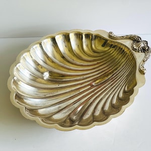 May include: A silver-plated serving dish shaped like a seashell with a decorative handle.