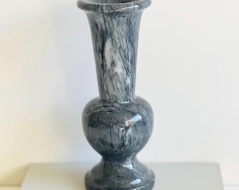 May include: A gray marble vase with a round body and a flared opening. The vase has a smooth, polished finish.