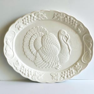 May include: White ceramic serving platter with a raised design of a turkey and grapes around the edge.