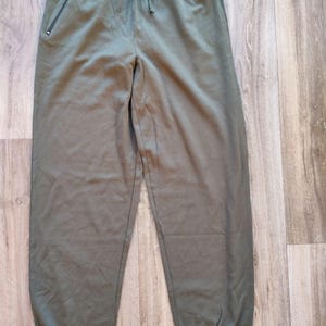 May include: Olive green sweatpants with a drawstring waist and zippered pockets. The pants have a relaxed fit and cuffed ankles. The fabric appears to be a soft, comfortable material, suitable for casual wear.