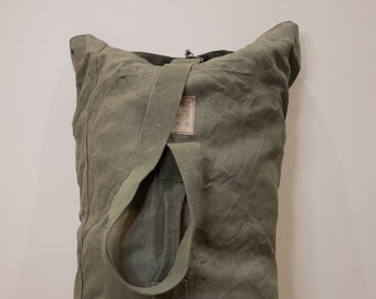 May include: A large, green canvas duffel bag with a single strap and a small, rectangular tag that reads "U.S. ARMY".