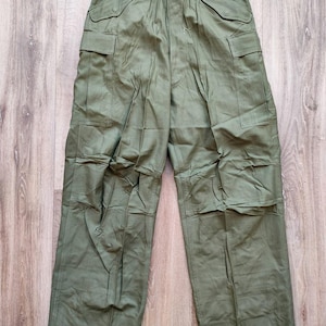 Puede incluir: Pantalones cargo verde oliva con múltiples bolsillos y cierre de botón y cremallera. Los pantalones tienen cintura alta y corte holgado. La tela parece ser un material duradero, posiblemente de estilo militar.