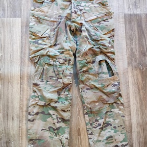 May include: Camouflage cargo trousers with multiple pockets and a knee pad design. The trousers are in a green, brown, and tan colour scheme.