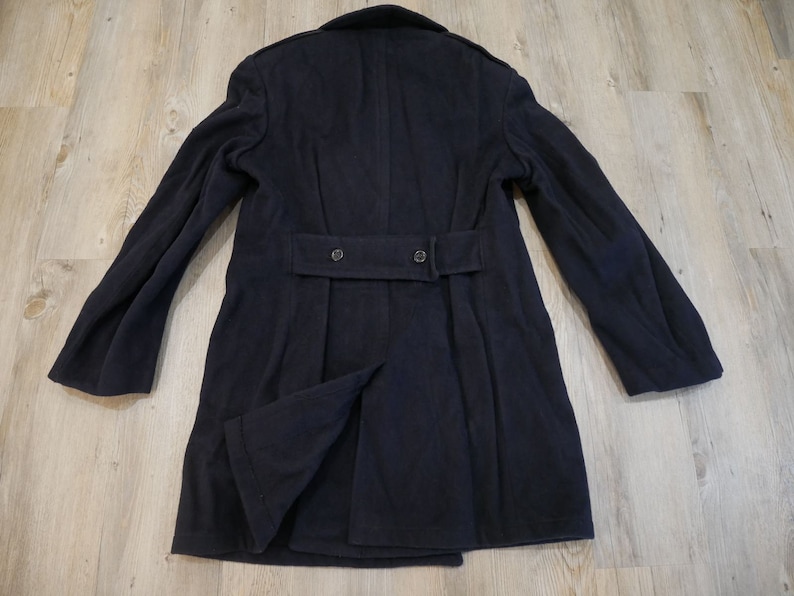 May include: A dark blue wool peacoat with a belt and two buttons on the back.