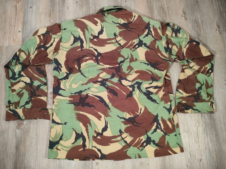 May include: A long-sleeved, button-up shirt with a camouflage pattern. The shirt is made from a cotton blend and has a relaxed fit.
