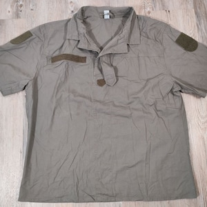 Op de afbeelding: Een kort mouwig, olijfgroen utility shirt met twee klepzakken op de borst en twee klittenband patches op de mouwen.