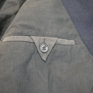 May include: Close-up of a black jacket with a single button on the inside pocket.
