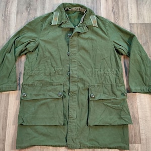 May include: A long-sleeved green jacket with a button-up front and two large pockets on the front. The jacket has a green and brown collar.