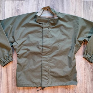 Puede incluir: Chaqueta verde oliva con cuello alto y mangas largas. La chaqueta tiene cierre de cremallera completa y un cordón en la parte inferior. Las mangas tienen puños elásticos. La chaqueta está hecha de un material ligero y resistente al agua.