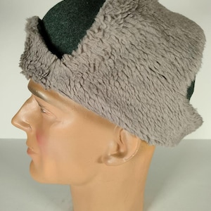 Könnte beinhalten: Ein dunkelgrüner Filzhut mit einem grauen Kunstfell-Ohrenschutz. Der Hut wird auf einem Mannequin-Kopf getragen.