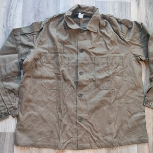Può includere: Una camicia da lavoro a maniche lunghe di colore verde oliva con chiusura a bottoni e due tasche sul petto.