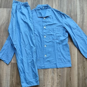 Peut inclure: Un ensemble de pyjama bleu clair, composé d'une chemise boutonnée avec une poche poitrine et d'un pantalon long. L'ensemble est en tissu léger et est posé sur une surface en bois.