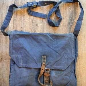 Può includere: Borsa messenger in tela blu con chiusura a patta e tracolla regolabile. La borsa presenta una chiusura con fibbia in pelle ed è di forma rettangolare. Realizzata in resistente materiale di tela.