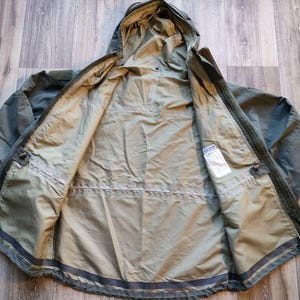 May include: Olive green hooded jacket with a full zipper and interior pockets. The jacket is open, revealing the interior lining and a tag. The jacket is made of a lightweight material, suitable for outdoor activities.