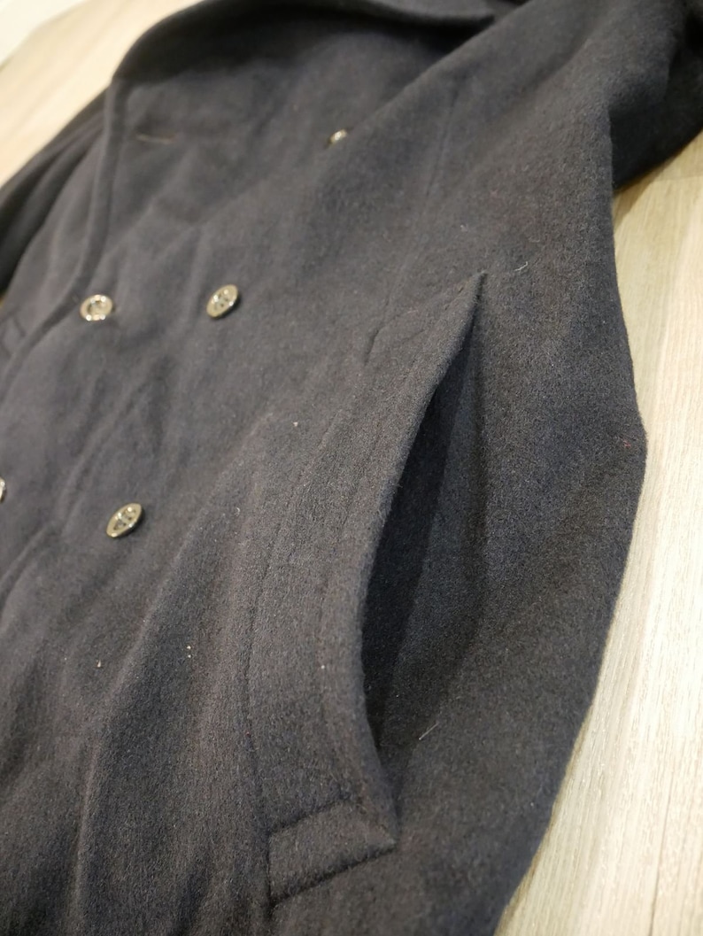 May include: A black wool peacoat with a double breasted closure and a large pocket on the right side.