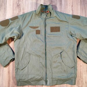 Peut inclure: Veste vert clair avec une fermeture éclair intégrale, deux poches avant et des écussons sur les manches et la poitrine. La veste a un col montant et une doublure vert foncé. La veste est faite d'un matériau durable.