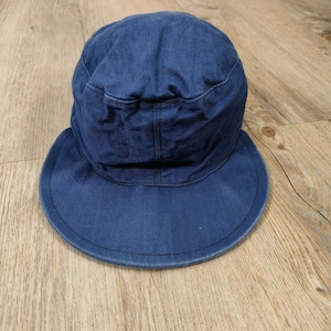 May include: A dark blue denim work cap with a wide brim. The cap is made of a thick, durable fabric and has a simple design.
