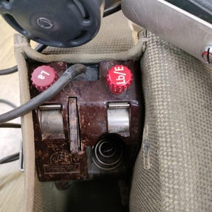 May include: Close-up of a brown vintage radio transmitter with two red knobs labeled "L2" and "Lb/E". The transmitter is in a canvas bag.