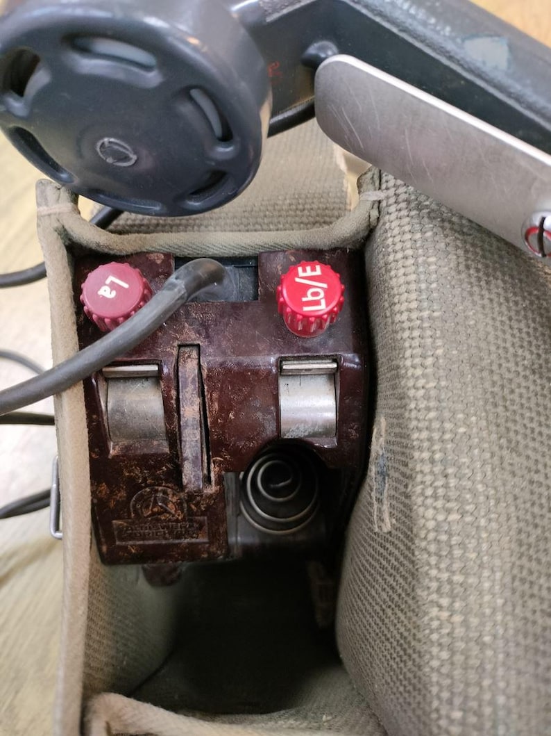 May include: Close-up of a brown vintage radio transmitter with two red knobs labeled "L2" and "Lb/E". The transmitter is in a canvas bag.