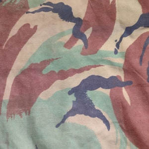 May include: Close-up of a camouflage fabric with a pattern of brown, green, and blue. The fabric has a textured surface and is made of a woven material.