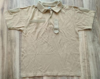 Peut inclure: Un polo à manches courtes de couleur beige avec un col boutonné et deux poches plaquées sur la poitrine. Le polo a une petite boucle en tissu sur le côté gauche du col.
