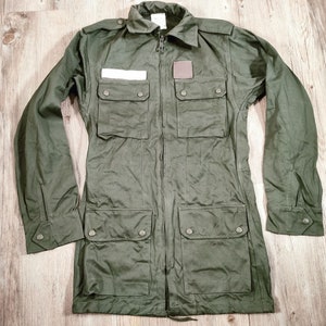 May include: A green utility jacket with a zipper closure, two large pockets on the front, and a small patch on the left chest.