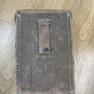 May include: A green canvas pouch with a brown leather strap and a flap closure. The pouch has a worn and faded appearance.