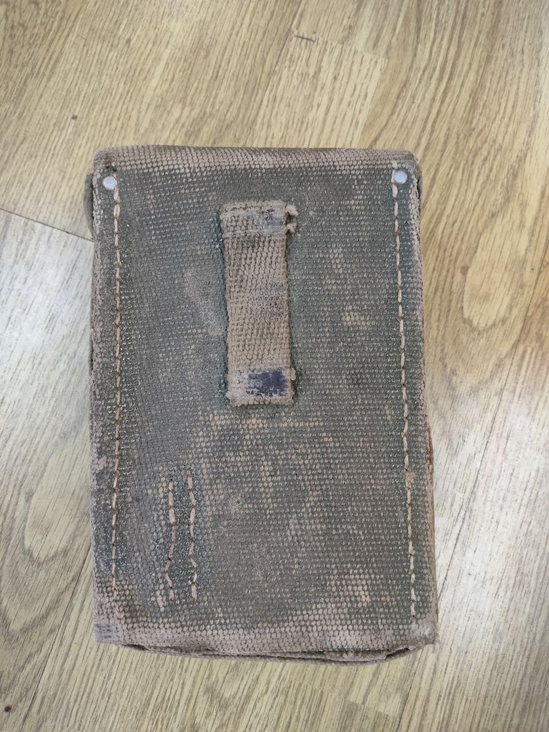 May include: A green canvas pouch with a brown leather strap and a flap closure. The pouch has a worn and faded appearance.