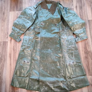 May include: A green rubberized raincoat with a double-breasted closure and a large collar. The raincoat has a faded appearance and several buttons.