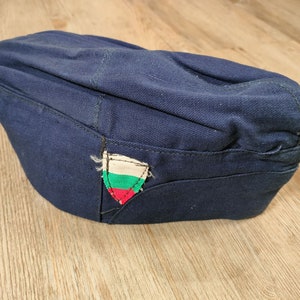 Könnte beinhalten: Eine dunkelblaue Militärkappe mit einem kleinen gestickten Aufnäher mit der bulgarischen Flagge.