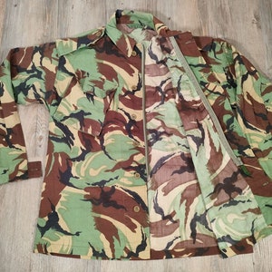 May include: A camouflage-patterned shirt with a zip closure and button-up front. The shirt has two large pockets on the front and a green zip pull.