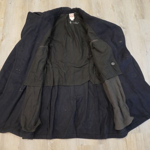 May include: A navy blue wool peacoat with a black lining and a single button closure. The coat is unbuttoned and the lining is visible. The coat has two pockets on the outside and two pockets on the inside.