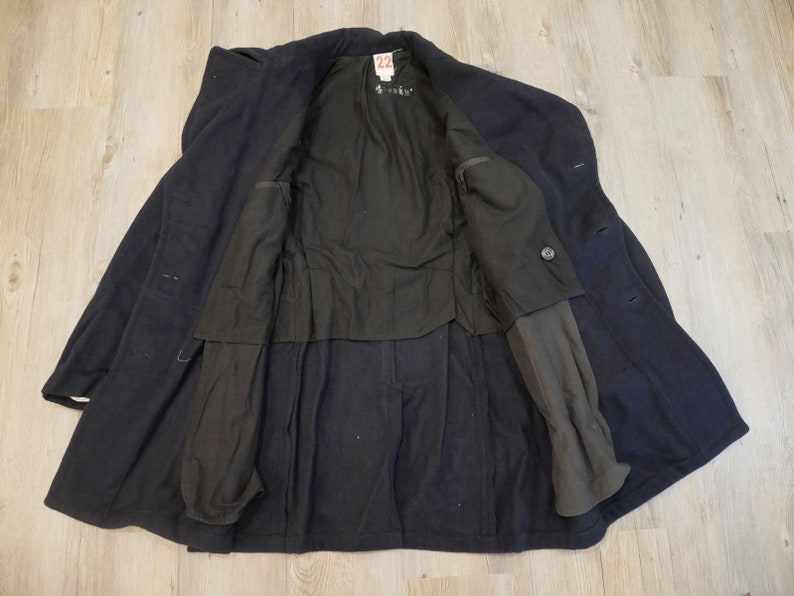 May include: A navy blue wool peacoat with a black lining and a single button closure. The coat is unbuttoned and the lining is visible. The coat has two pockets on the outside and two pockets on the inside.