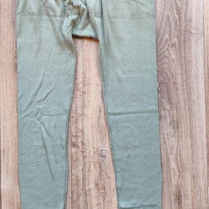 May include: Pale green thermal underwear bottoms. The trousers have a ribbed texture and an elasticated waistband. The cuffs at the ankles are ribbed. The garment is made of a soft, breathable material.